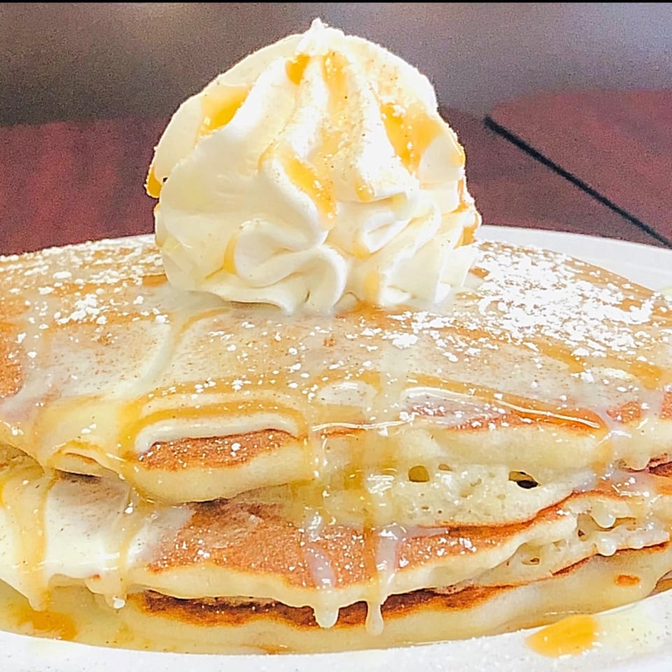 Stack of Sweet Desert Cafe pancakes topped with whipped cream, syrup, and powdered sugar.