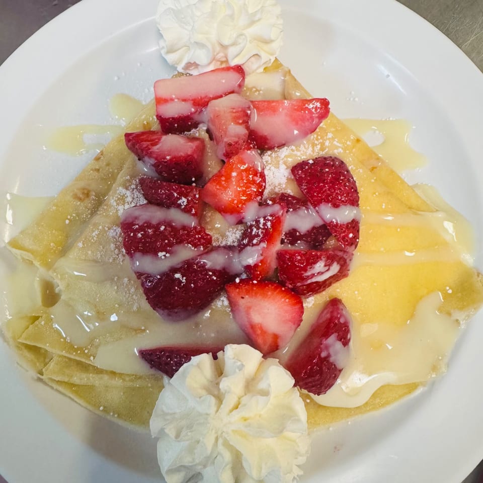 A Sweet Desert Cafe crepe with strawberries, whipped cream, and a sweet drizzle on a white plate.