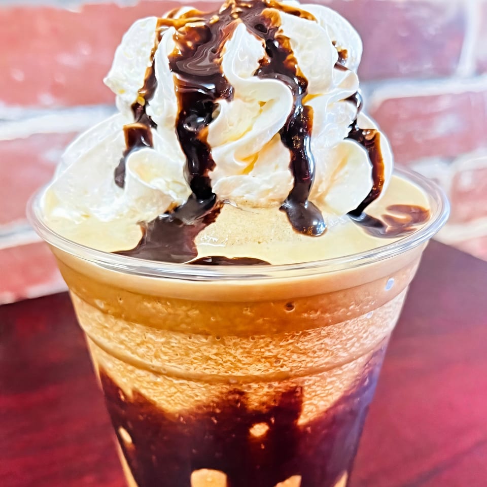Sweet Desert Cafe's iced coffee with whipped cream and chocolate drizzle against a brick wall.
