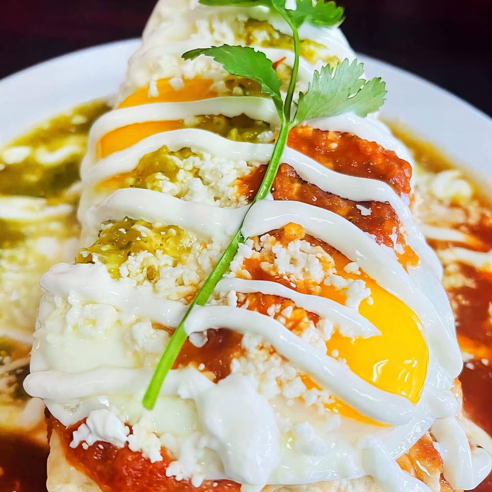 Breakfast burrito topped with two fried eggs, green and red salsa, sour cream, and cilantro.