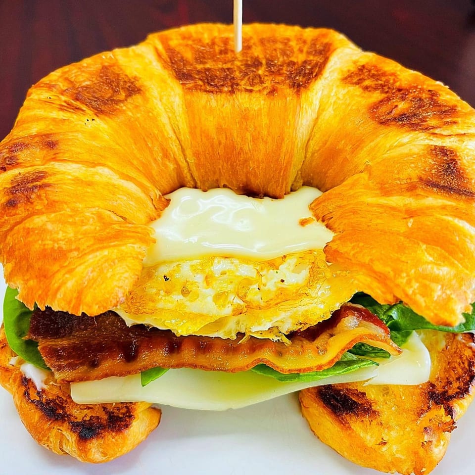 Sweet Desert Cafe's breakfast croissant with bacon, egg, cheese, and spinach on a white plate.